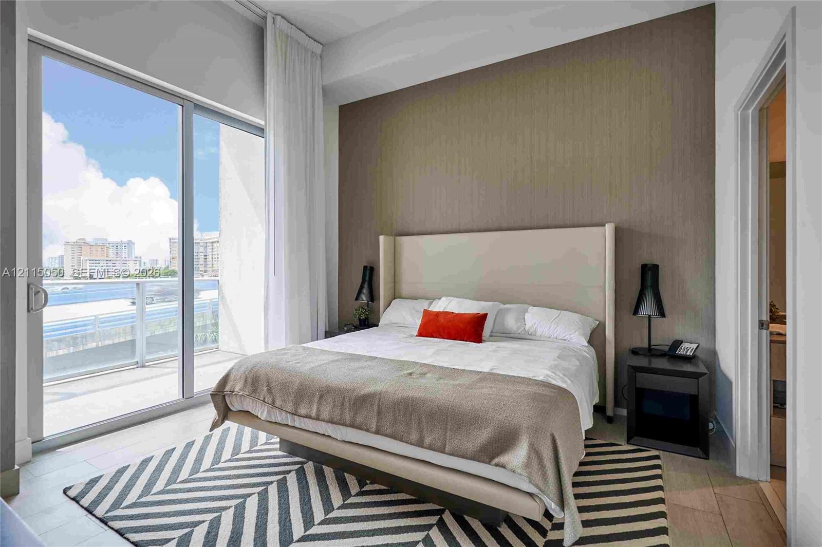 Floor-to-ceiling sliding glass door, private balcony, neutral-toned accent wall, and light-colored tile flooring