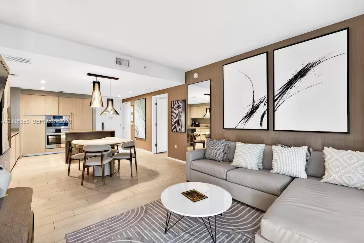 Living area featuring light wood-finish flooring, vertical slat accent wall, and built-in stainless steel wall oven Living area featuring light wood-finish flooring, vertical slat accent wall, and built-in stainless steel wall oven