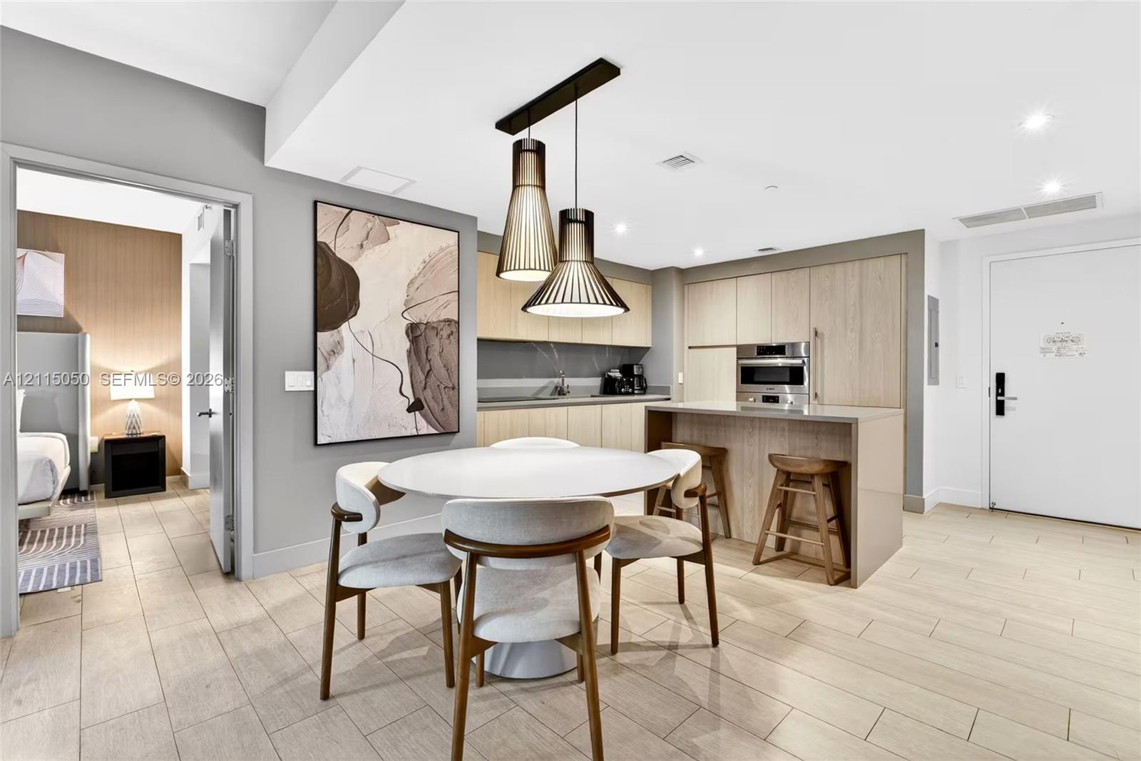 Kitchen featuring wood-finish cabinetry, stone-surface counters, a waterfall-edge kitchen island, integrated stainless steel appliances, and tiered metal pendant lighting over tile flooring
