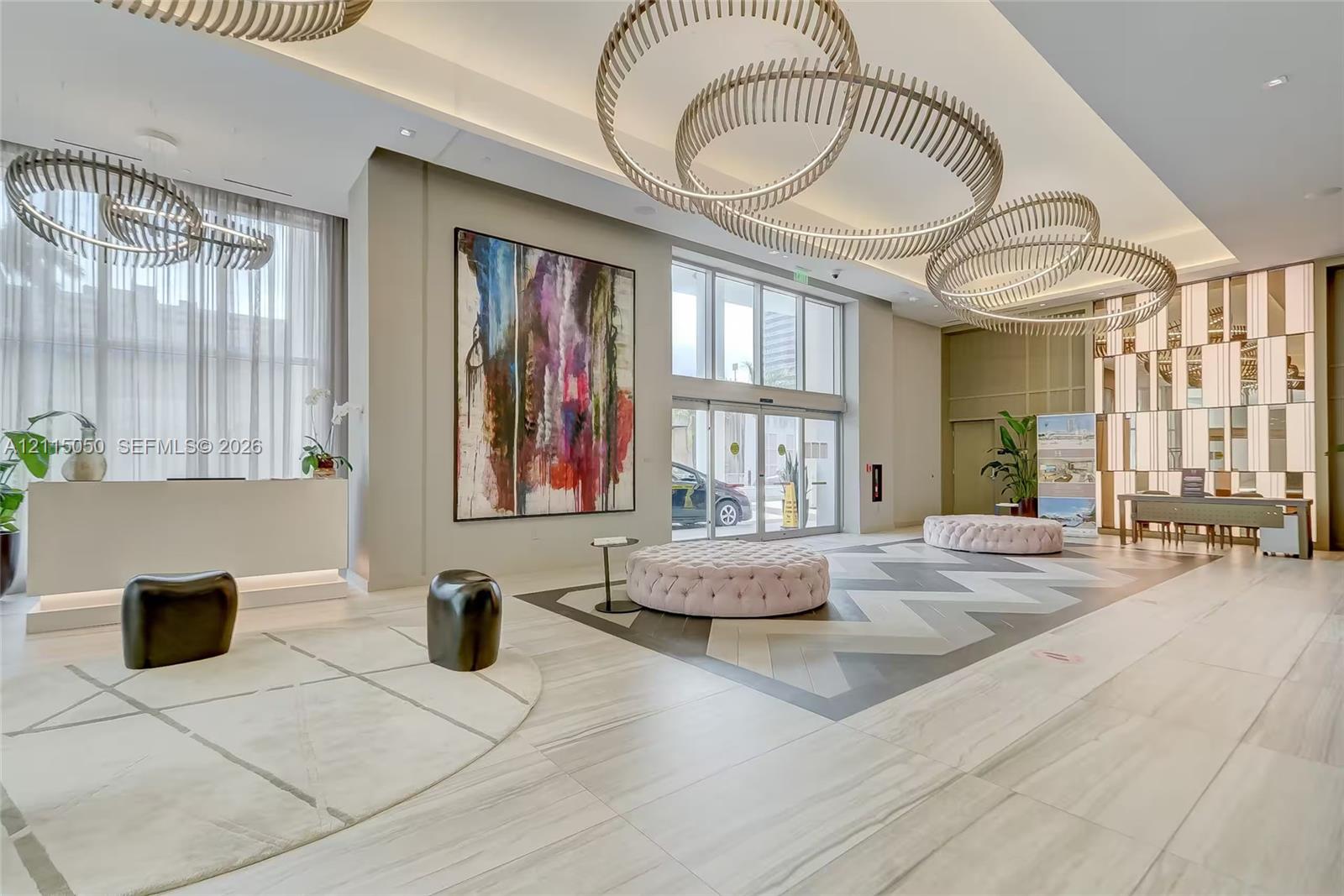 Lobby featuring floor-to-ceiling windows, oversized circular pendant lighting, large-format tile flooring with geometric inlay, and a built-in reception desk