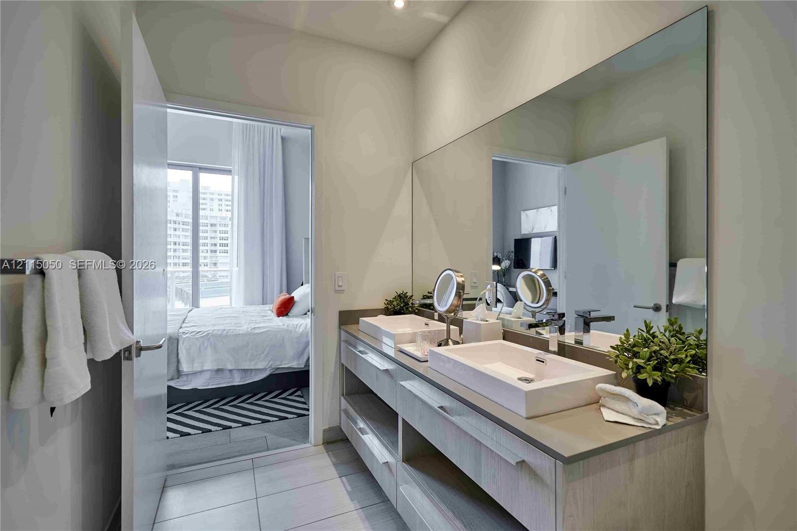 Double vanity featuring rectangular vessel sinks, stone-finish countertops, light-toned wood cabinetry, and a full-width wall mirror
