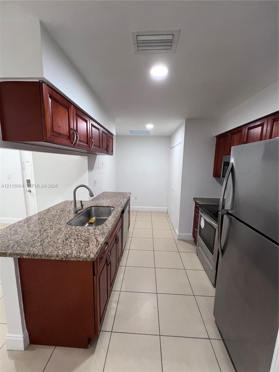 Kitchen featuring cherry-finish cabinetry, stone-composite countertops, stainless steel appliances, a recessed stainless steel sink, and ceramic tile flooring