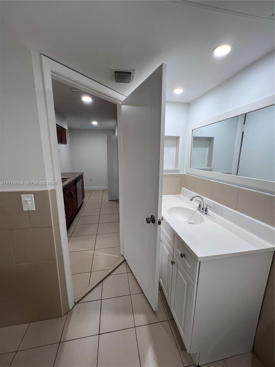 Bathroom vanity with a white cabinet, integrated sink, chrome faucet, and rectangular mirror, featuring tile flooring and tile wall accents