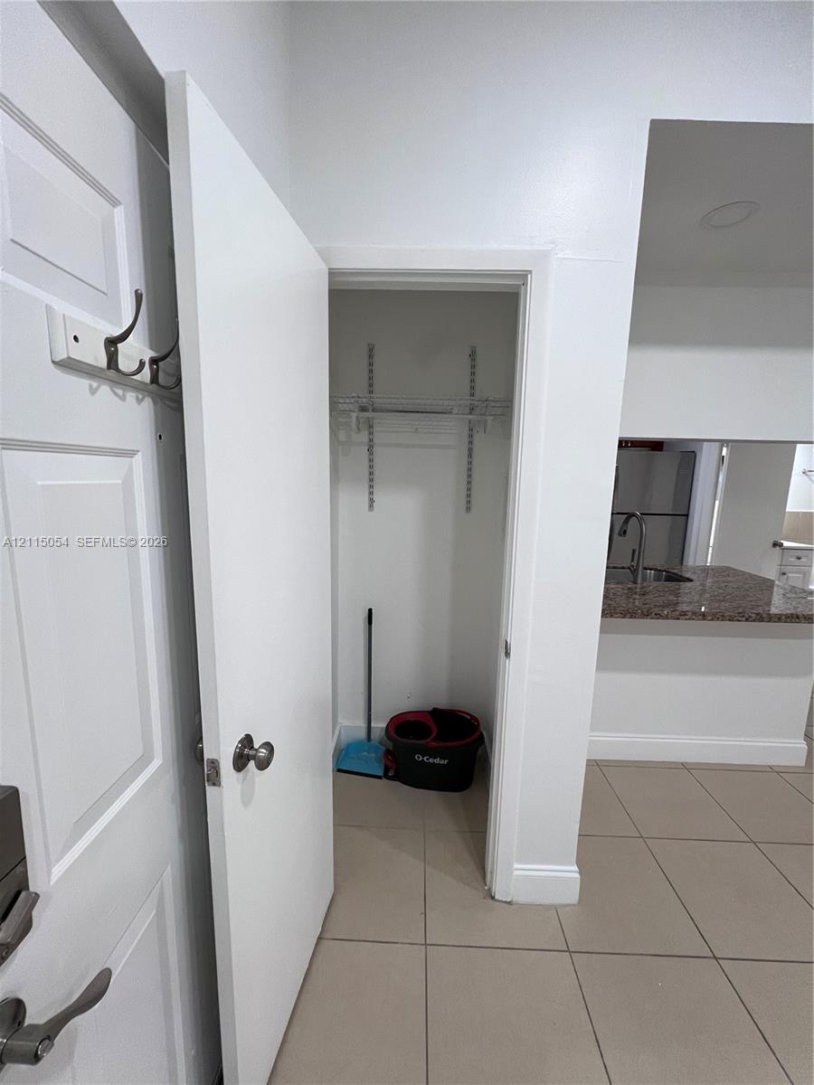 Storage closet featuring built-in shelving, tile flooring, and a wall-mounted hook rack