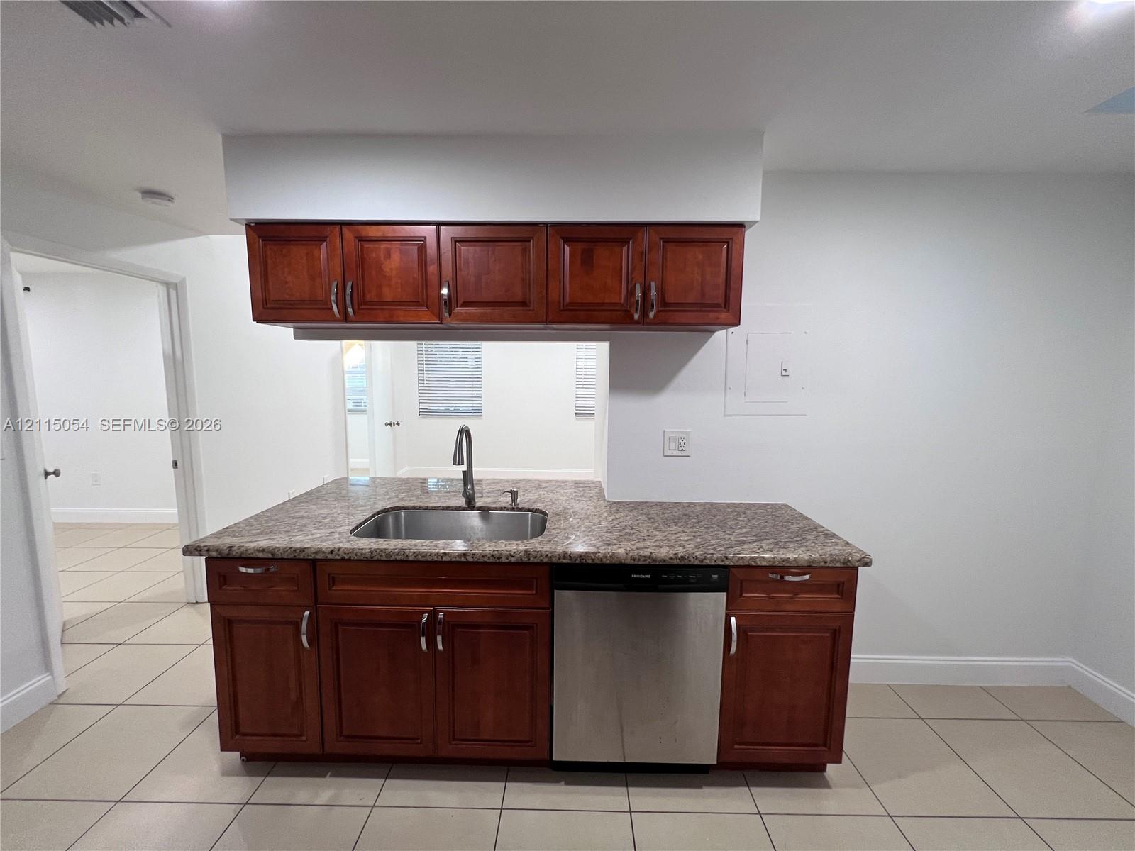 Kitchen cabinetry featuring rich wood-toned finish, stone-composite countertop, stainless steel undermount sink with arched faucet, and built-in stainless steel dishwasher