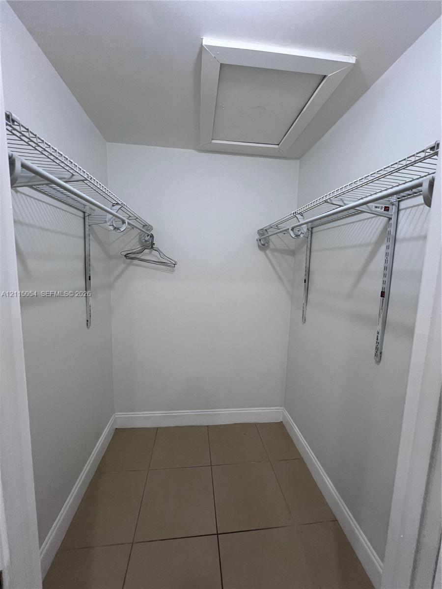 Storage area featuring ceramic tile flooring, dual-level wire shelving, and attic access panel
