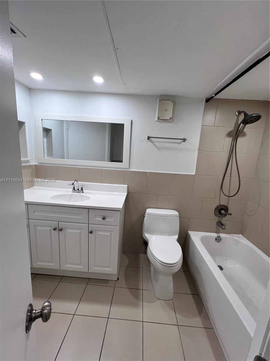 Bathroom featuring a white vanity cabinet with an integrated sink and countertop, large rectangular mirror, tile flooring, and a bathtub with a wall-mounted shower head and tile surround