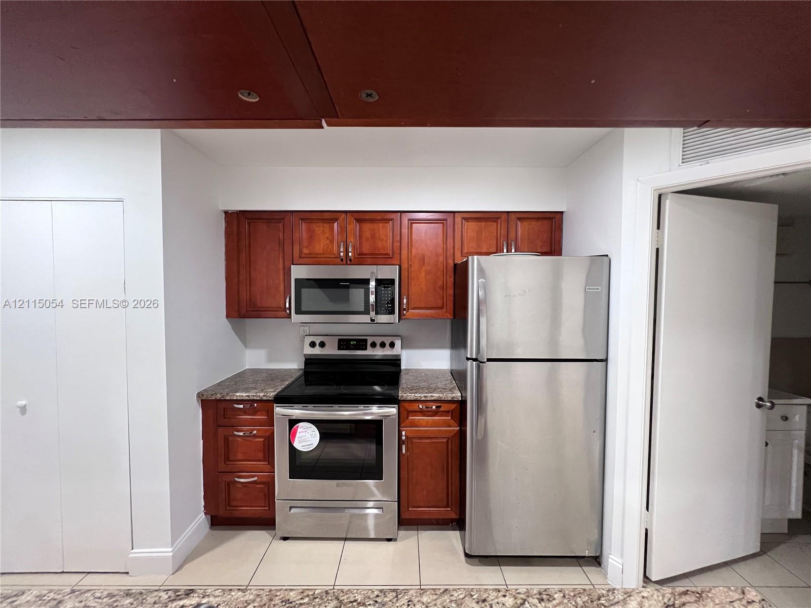Kitchen featuring wood-finish cabinetry, stone-patterned countertops, stainless steel appliances, and tile flooring