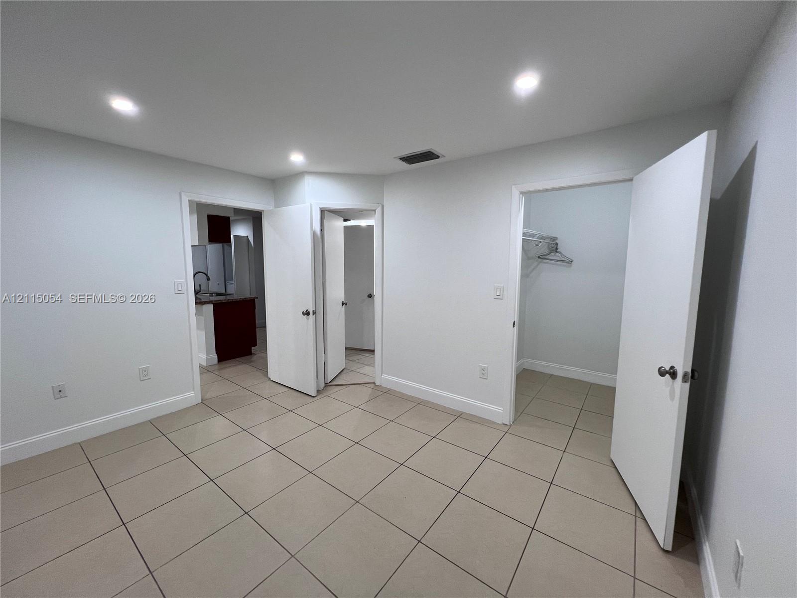 Neutral-toned tile flooring, recessed ceiling lighting, and multiple interior doorways with built-in closet shelving