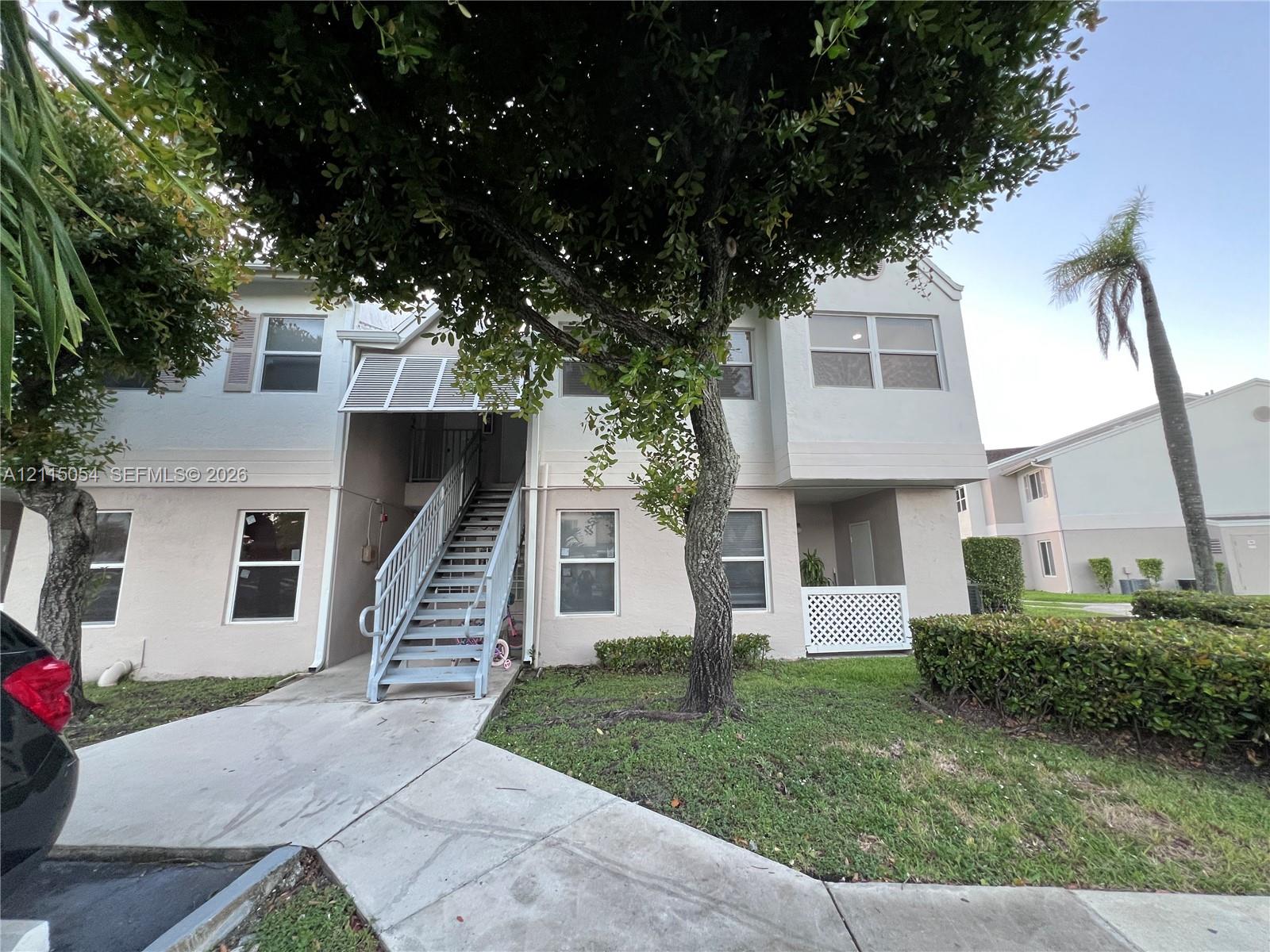 Two-story stucco exterior featuring a metal staircase, covered landing, decorative lattice screen, and mature landscape