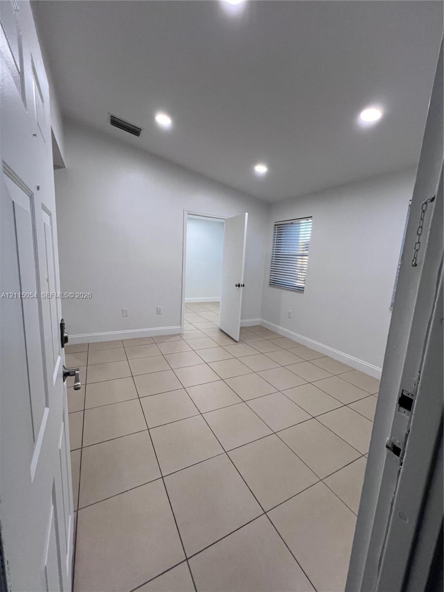 Interior room featuring large-format ceramic tile flooring, recessed ceiling lighting, and a window with horizontal blinds