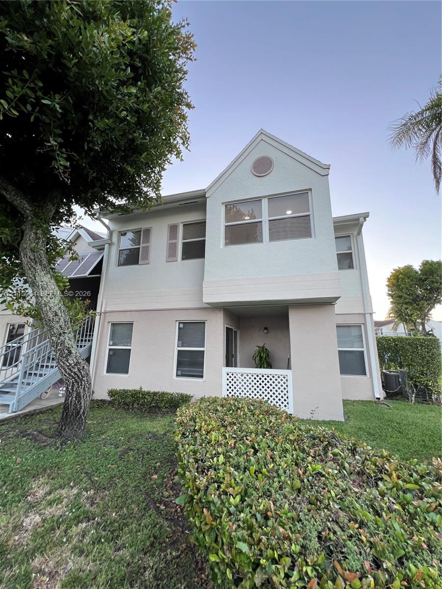 Two-story exterior featuring a light-toned stucco facade, dual-pane windows, a covered ground-level patio with lattice railing, and metal staircase access