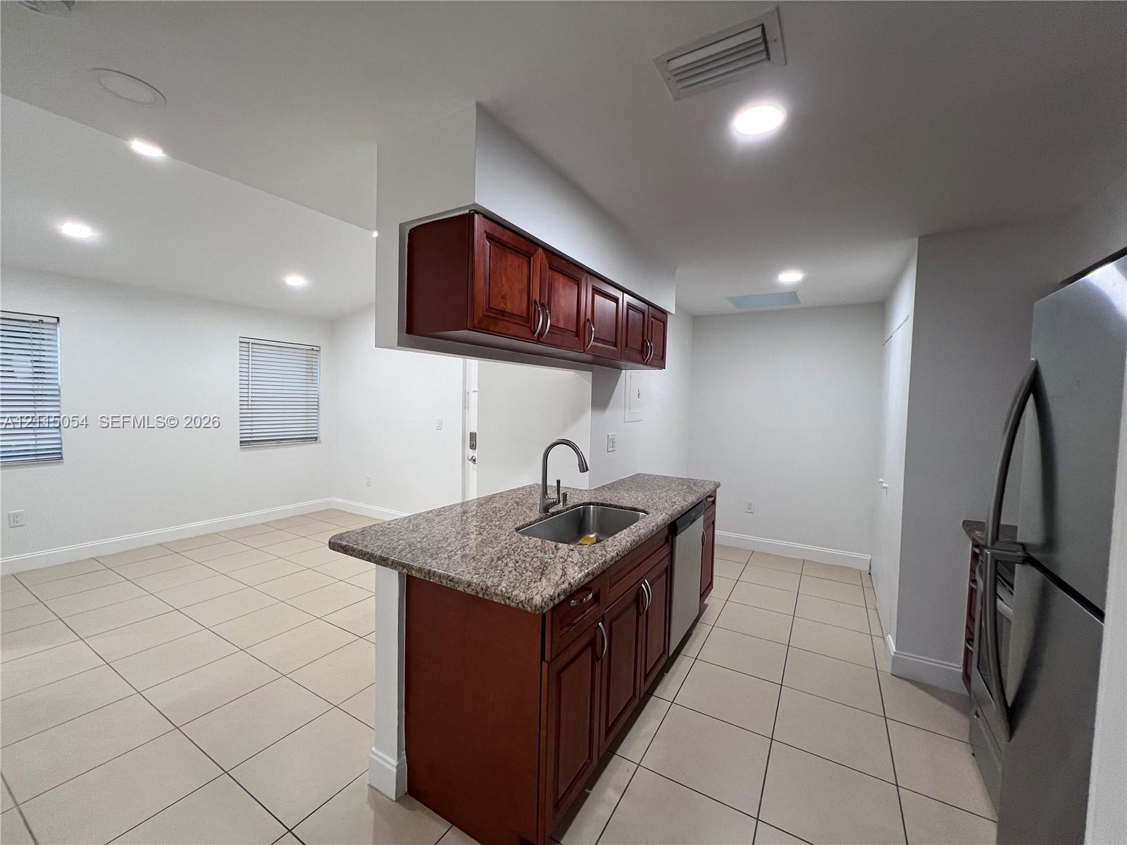 Kitchen featuring an island with a stone-finish countertop, stainless steel undermount sink, recessed lighting, tile flooring, and wood-finish cabinetry