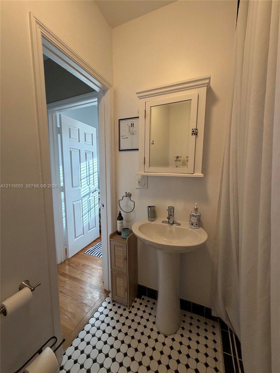 Pedestal sink with polished chrome faucet, wall-mounted medicine cabinet with mirror, and black-and-white penny tile flooring