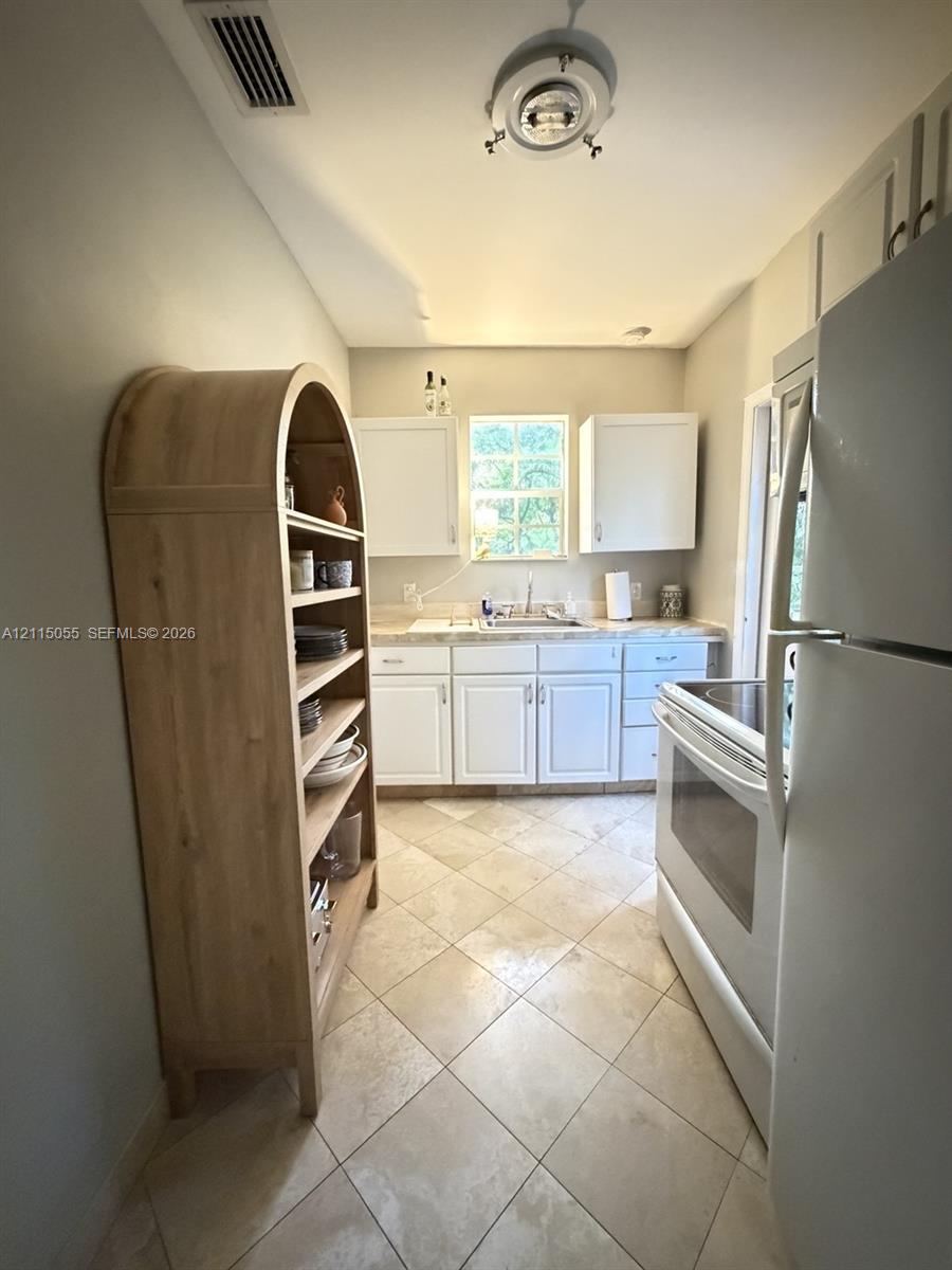 Kitchen featuring white shaker-style cabinetry, neutral-toned countertops, tile flooring laid on a diagonal, and stainless steel sink basin
