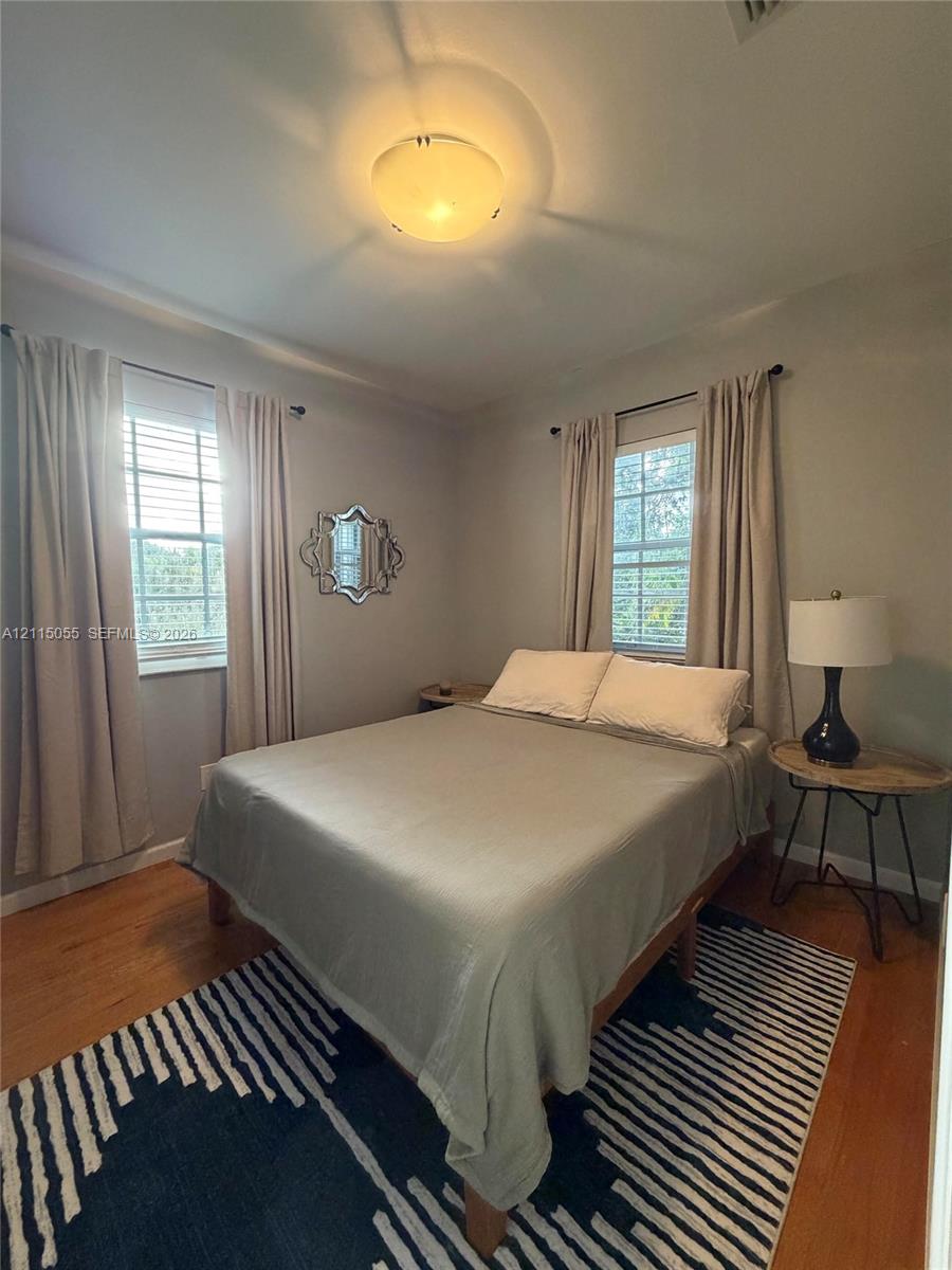 Bedroom featuring wood-finish flooring, two windows with double-hung frames, and a flush-mount ceiling light fixture