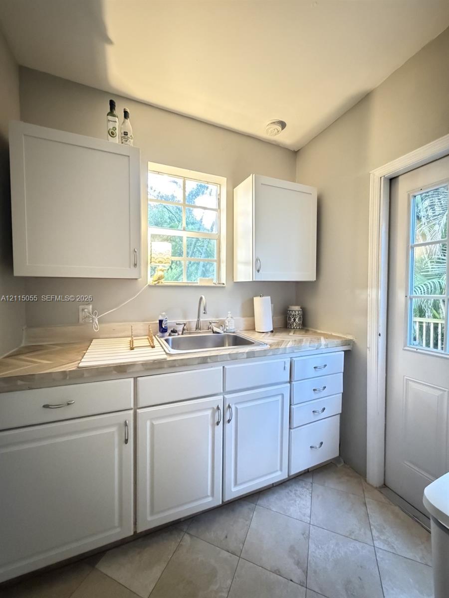 White cabinetry featuring shaker-style doors, herringbone-patterned laminate countertops, undermount stainless steel sink, tile flooring, and a glass-paneled exterior door