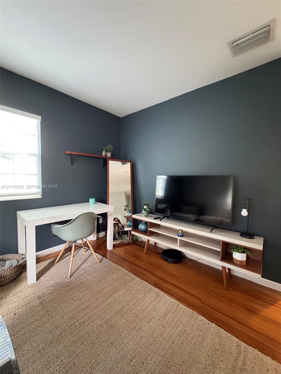 Room featuring dark accent wall, wood-finish flooring, and window with white horizontal blinds