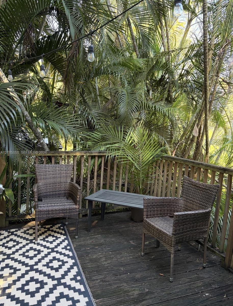 Outdoor deck featuring wood planking, vertical wood balustrades, and overhead string lighting, surrounded by mature palm trees