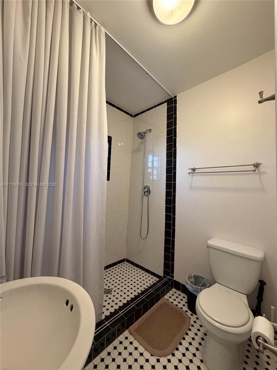 Full bathroom featuring a shower stall with white wall tile, a hand-held shower fixture, and a black-and-white patterned tile floor