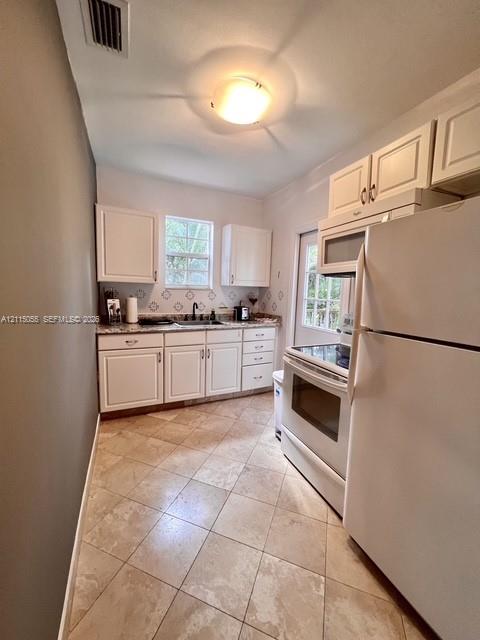 Kitchen featuring white cabinetry, patterned backsplash tile, stone-finish countertops, diagonal tile flooring, and integrated white appliances