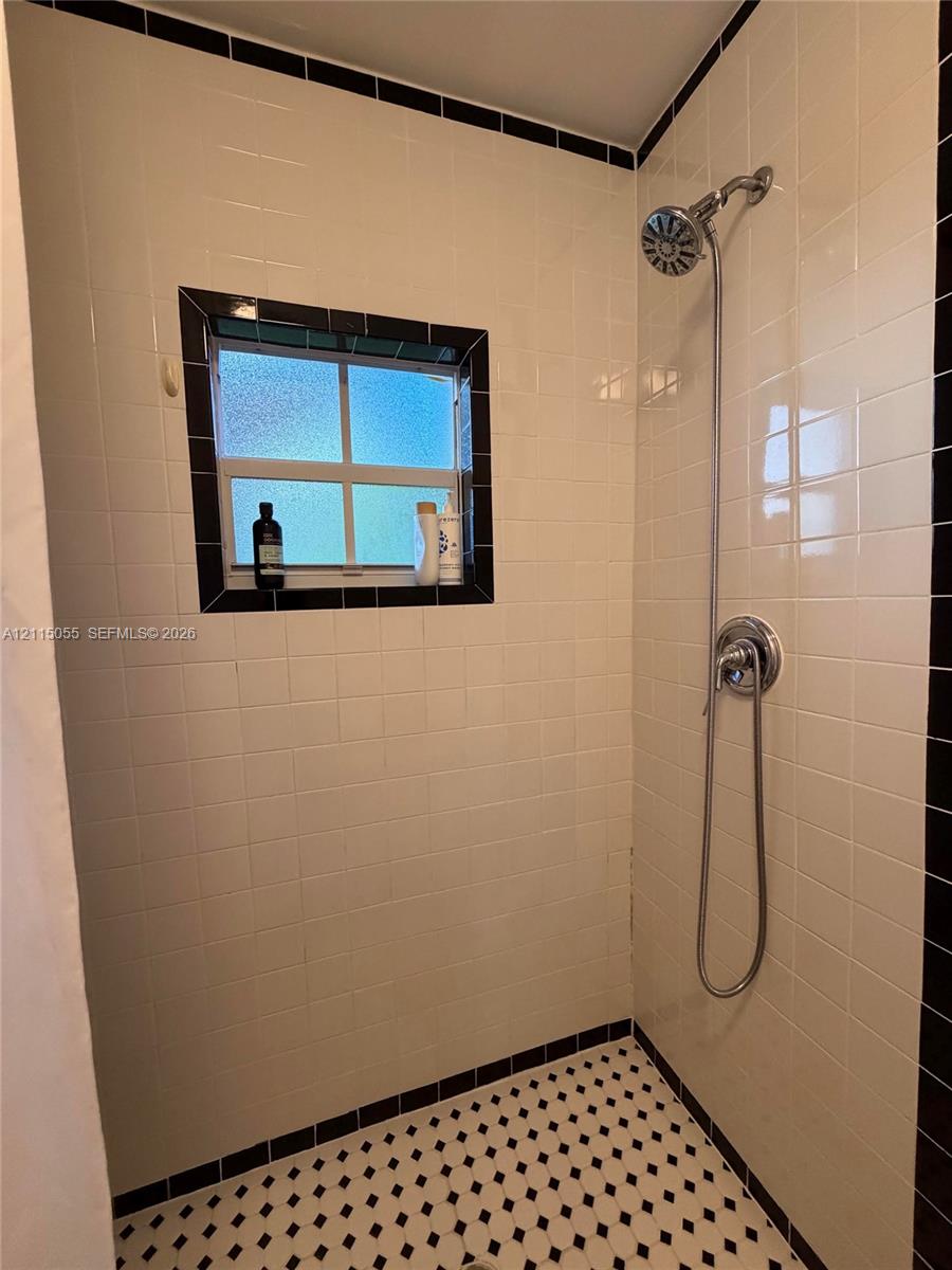 Walk-in shower featuring white subway wall tile with black accent trim, a handheld showerhead, a recessed window, and geometric patterned floor tile