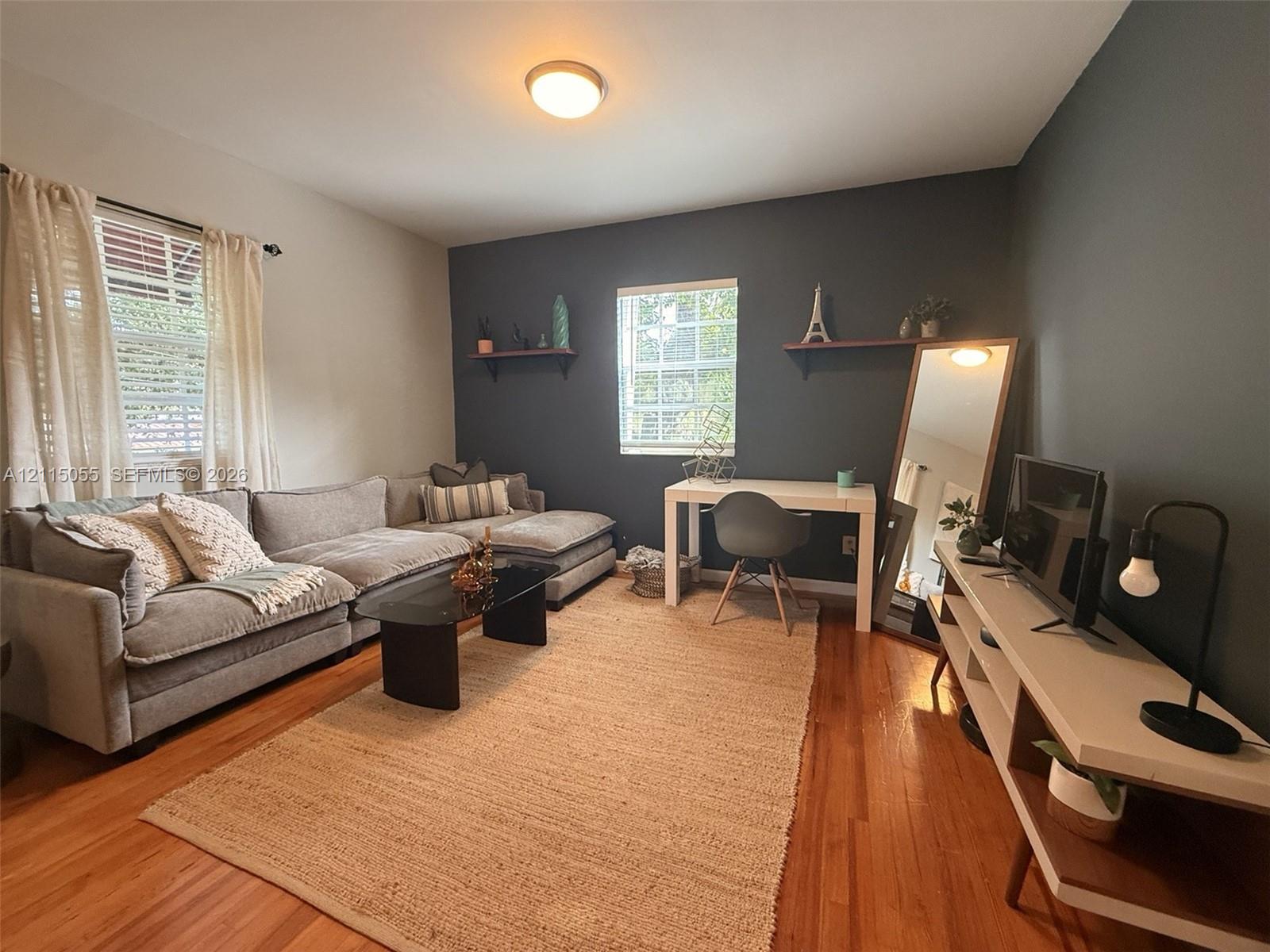 Interior space featuring wood-finish flooring, charcoal accent wall, two fixed floating wall shelves, and multi-pane window