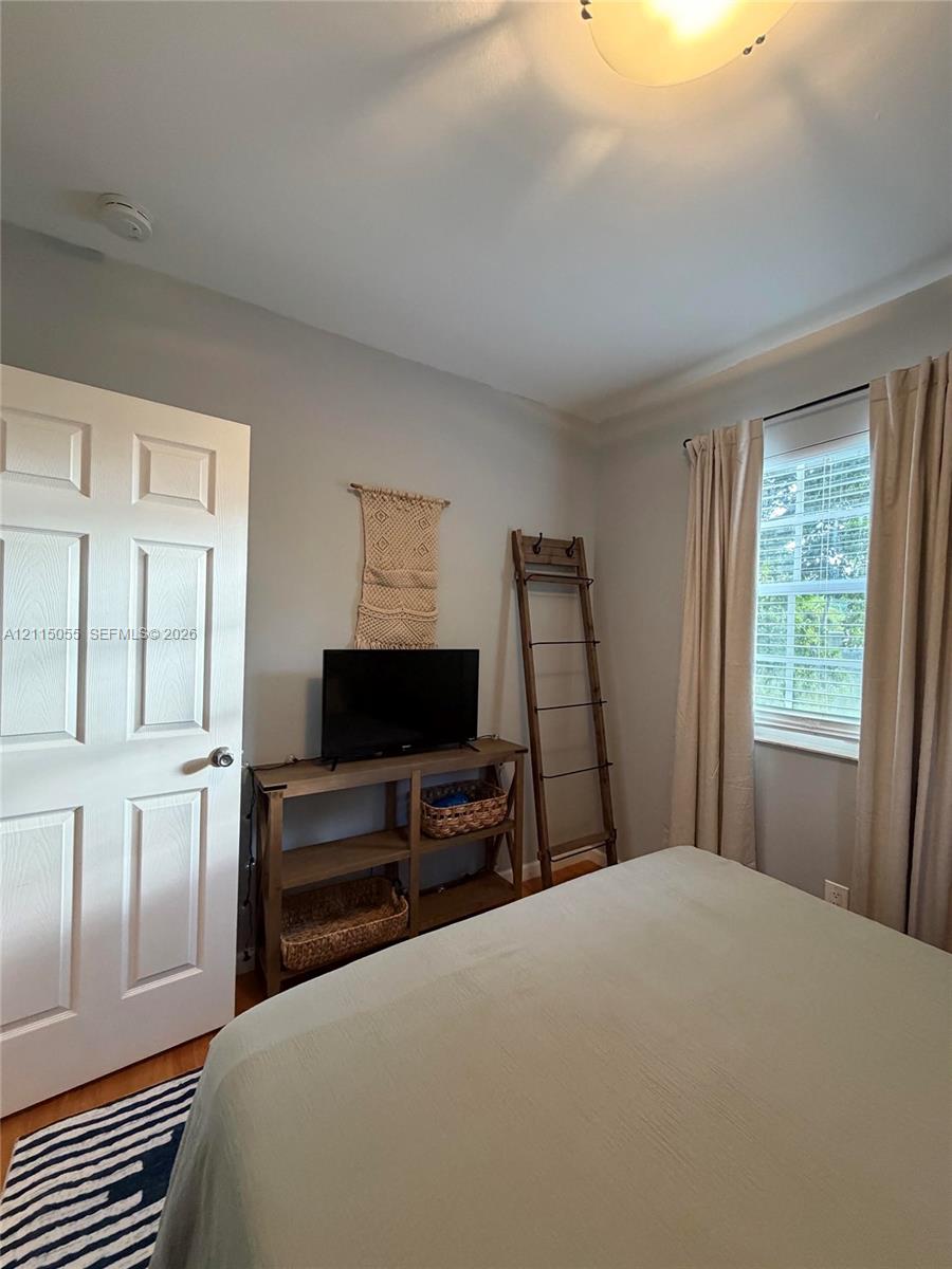 Neutral-toned interior featuring wood-finish flooring, a six-panel interior door, and a single-hung window with interior blinds