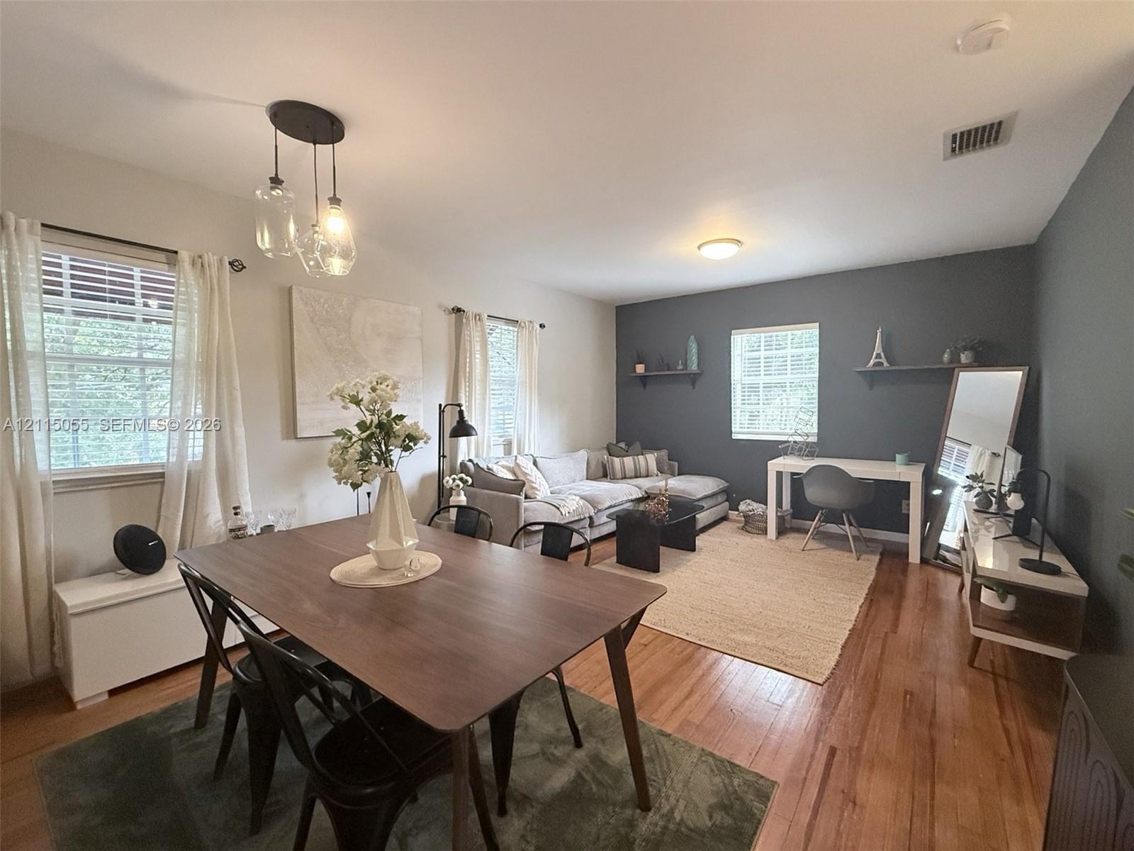 Living space featuring wood-finish flooring, a multi-light pendant fixture, and a dark-toned accent wall