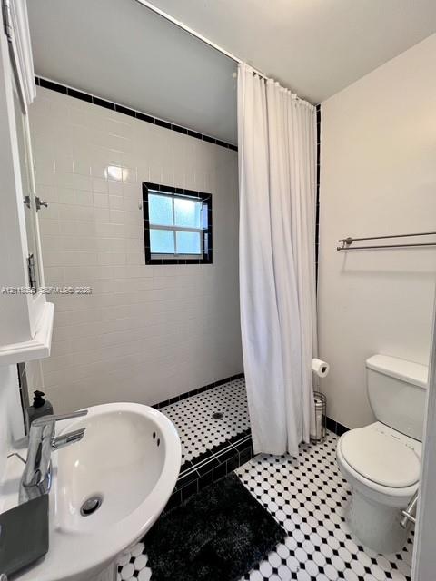 Bathroom featuring a pedestal sink with a chrome faucet, black and white hex floor tiling, white subway-style wall tiling with black accent trim, and a built-in recessed shower area with a window