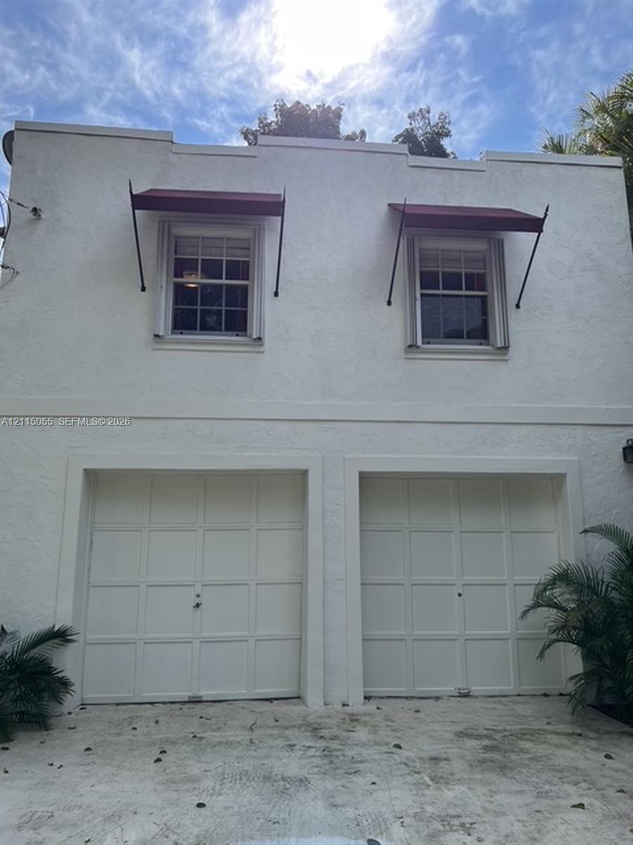 Stucco exterior facade featuring two garage bays, multi-pane windows, and metal awnings