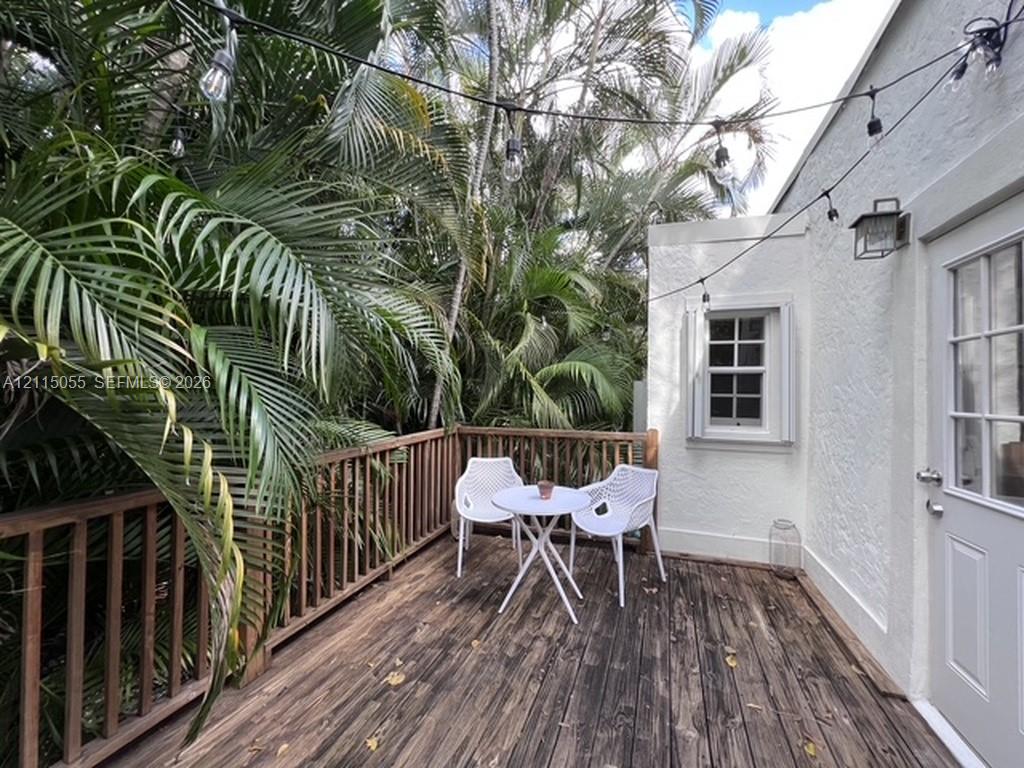 Exterior wood deck featuring a balustrade railing, white textured stucco siding, multi-pane window, and attached wall-mounted lantern light
