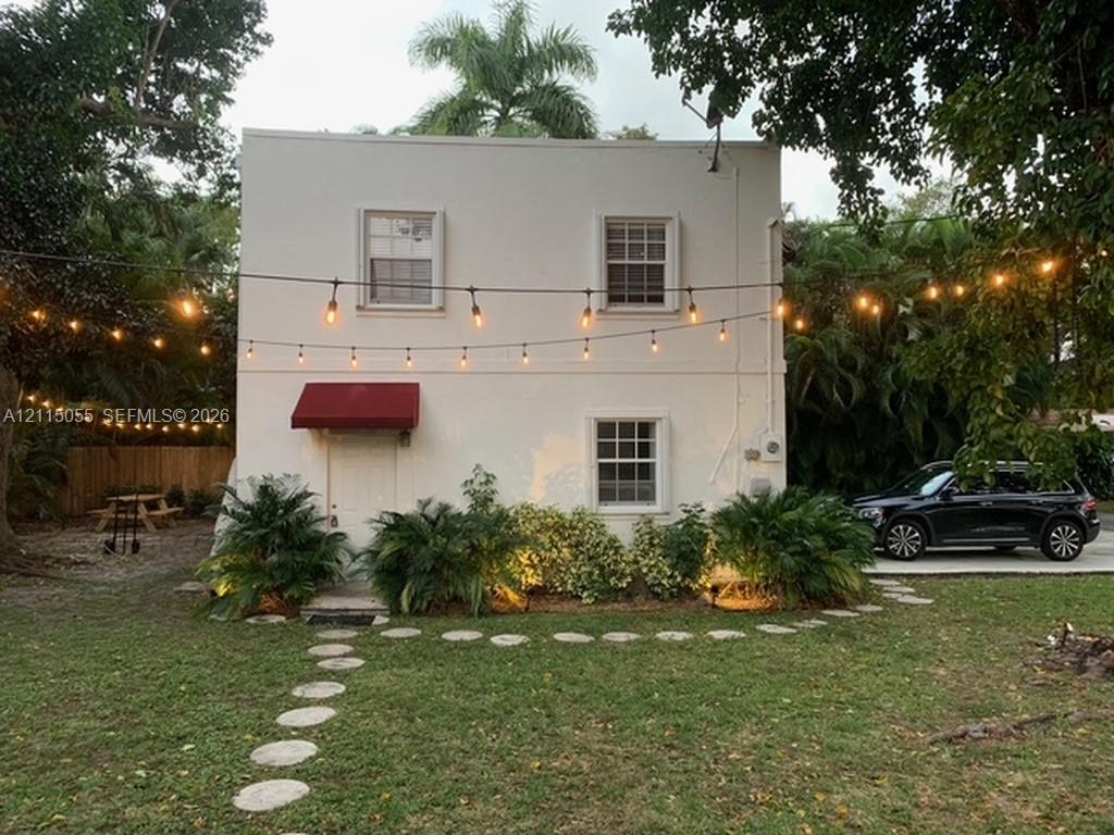 Two-story exterior featuring a smooth stucco finish, double-hung multi-pane windows, a red fabric awning, and a stone paver walkway