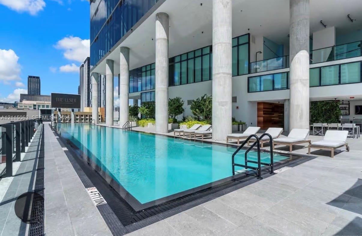 Swimming pool with concrete deck, structural pillars, and glass-paneled building exterior