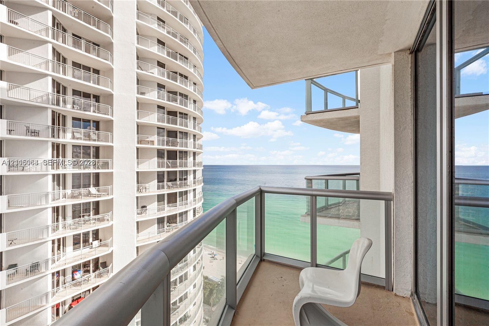 Covered balcony with glass and metal railings, concrete flooring, and panoramic ocean expanse