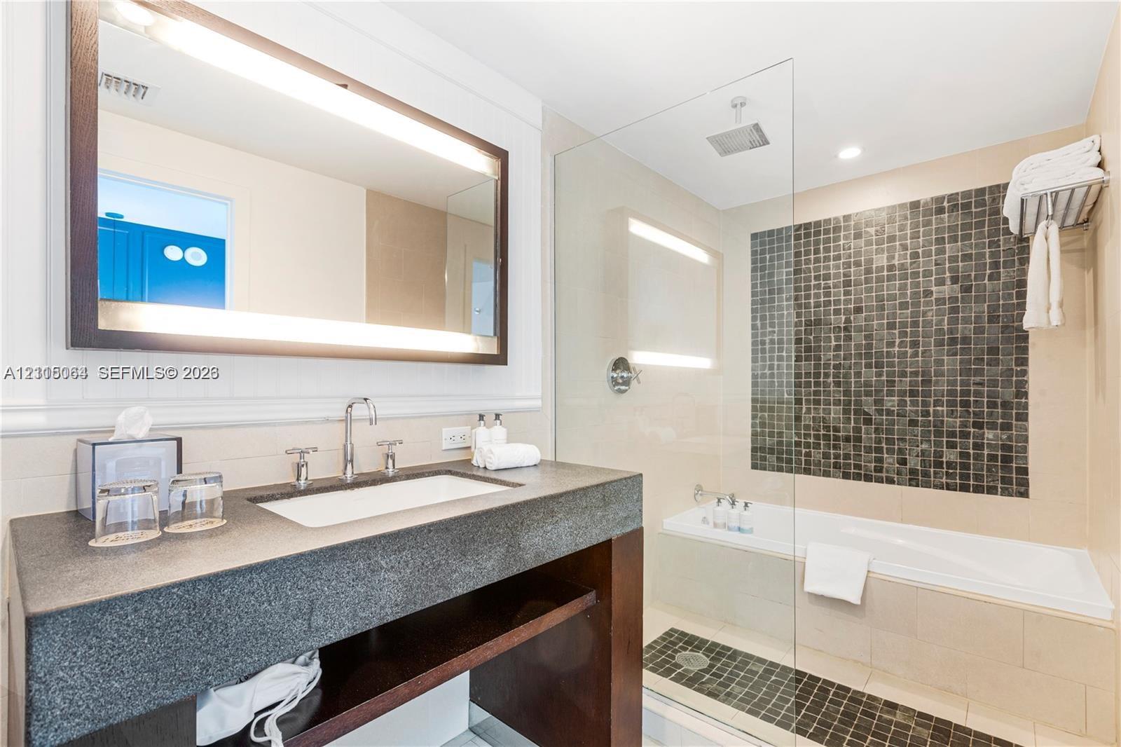 Bathroom featuring a floating dark wood vanity with a stone countertop, an integrated rectangular sink, a frameless glass-enclosed shower, and a built-in soaking tub with decorative tile inlay