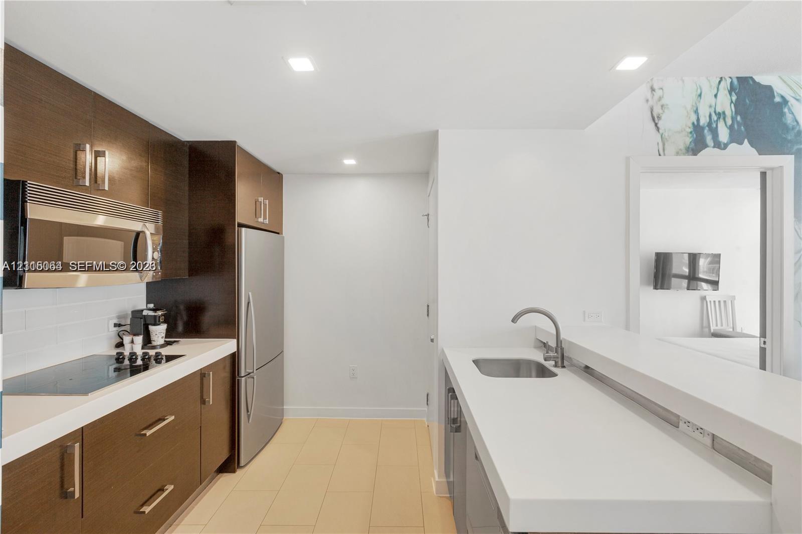Kitchen featuring wood-finish cabinetry, stainless steel appliances, flat-panel countertops, recessed lighting, and tile flooring