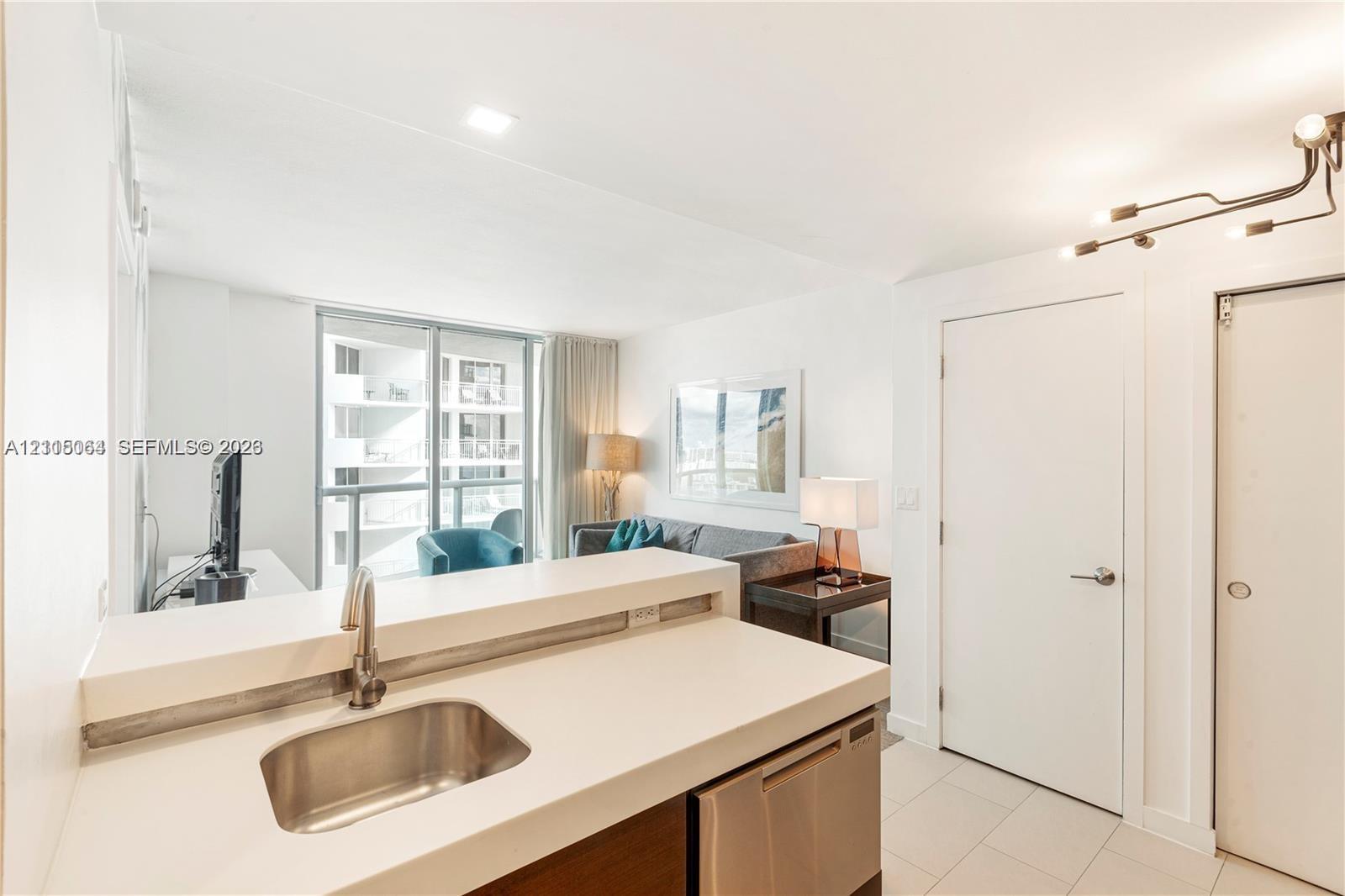 Kitchen featuring a white solid-surface countertop, stainless steel undermount sink with a gooseneck faucet, stainless steel dishwasher, modern multi-arm track lighting, and tile flooring