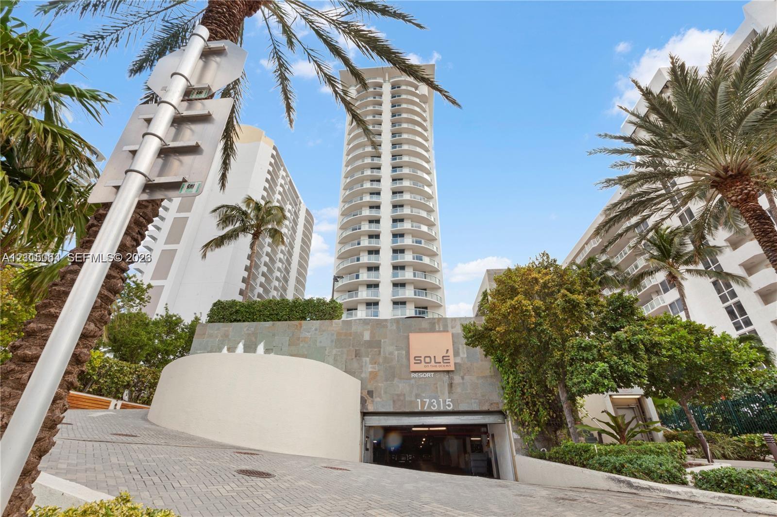 High-rise residential structure featuring a stone-clad facade, circular balcony design, and a paver-stone driveway leading to a covered parking garage entrance