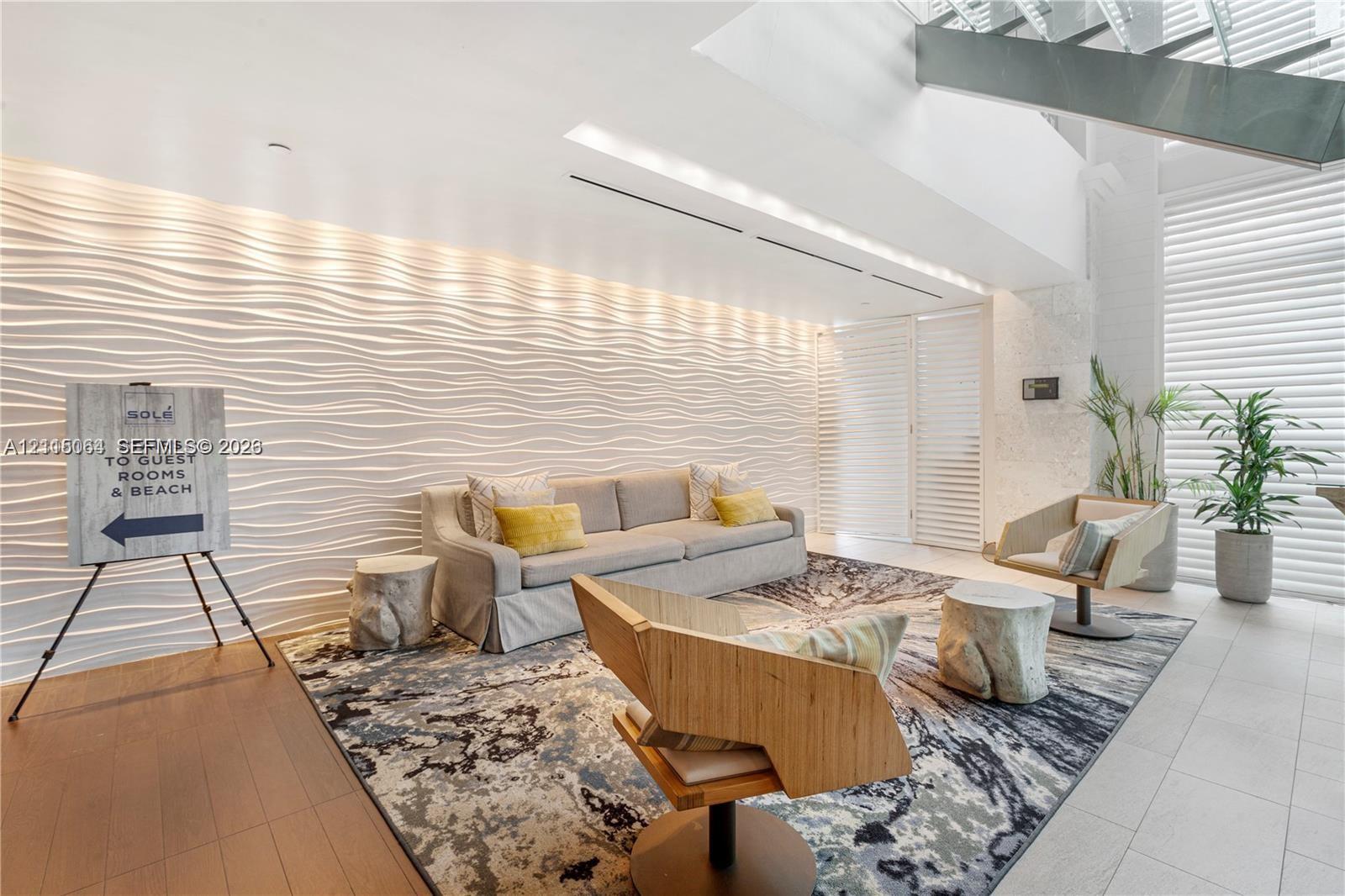 Textured, three-dimensional wave-pattern accent wall, high ceilings with integrated recessed lighting, metal-frame open-riser staircase, and floor-to-ceiling slatted window treatments
