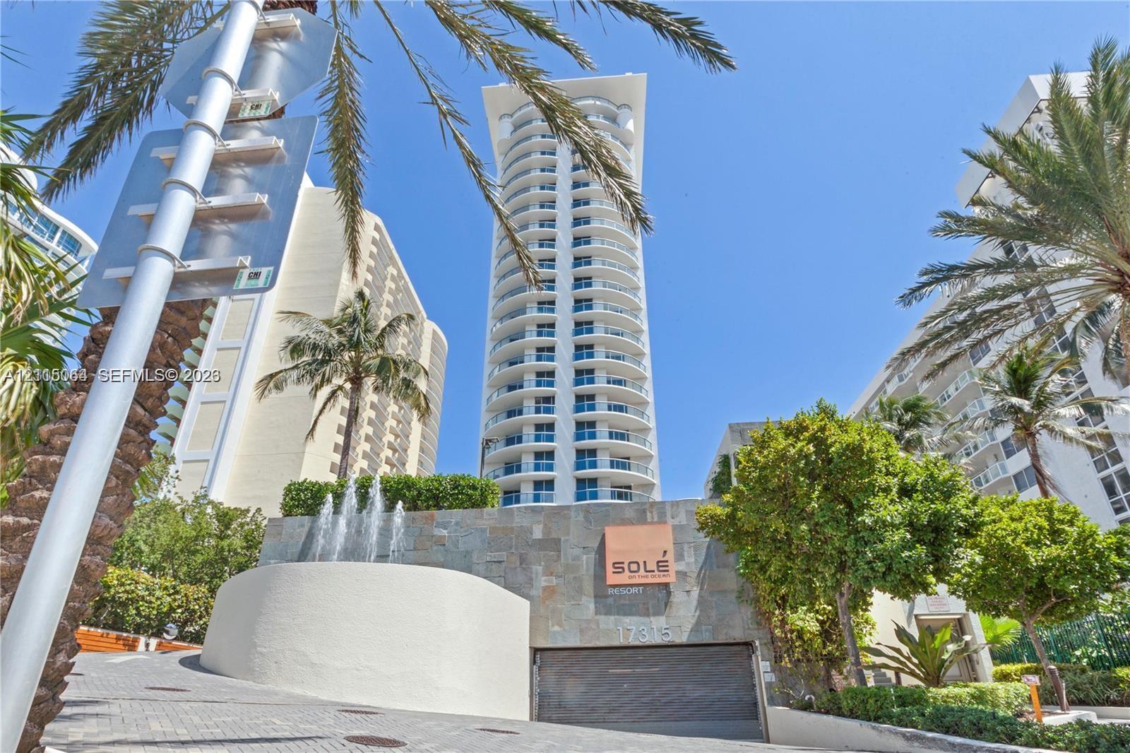 High-rise tower featuring rounded balconies, stone-clad entryway, decorative water fountain, and paved driveway