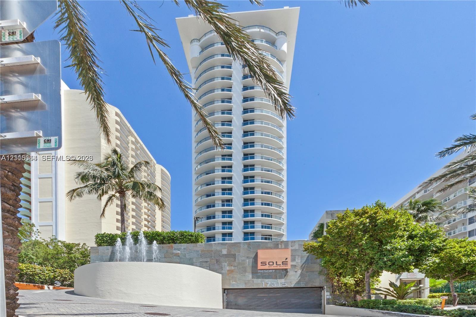 High-rise exterior featuring curved structural balconies, stone-clad entrance wall, and tiered water feature
