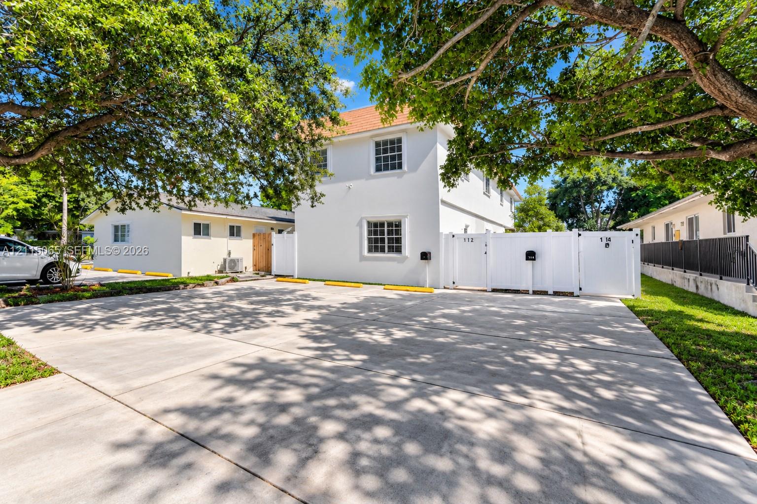 Concrete parking area featuring marked spaces, exterior white stucco siding, and white vinyl privacy fencing