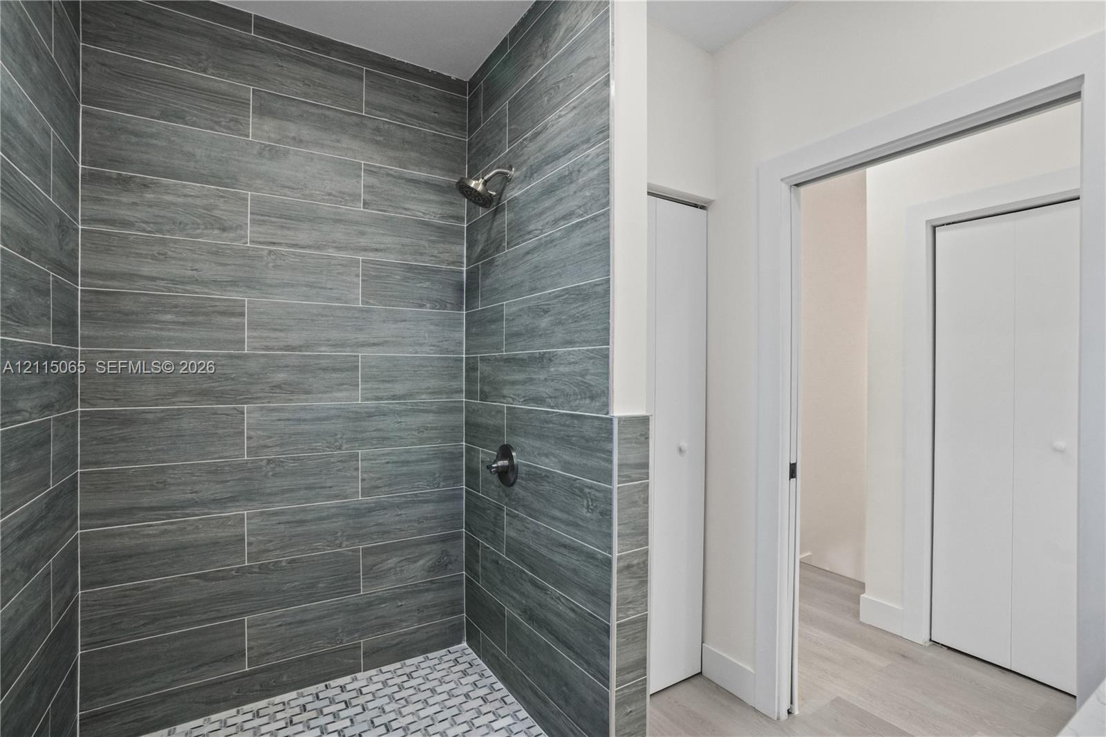 Walk-in shower featuring grey horizontal tile walls, a white penny-round mosaic tile floor, and a polished chrome showerhead with matching controls