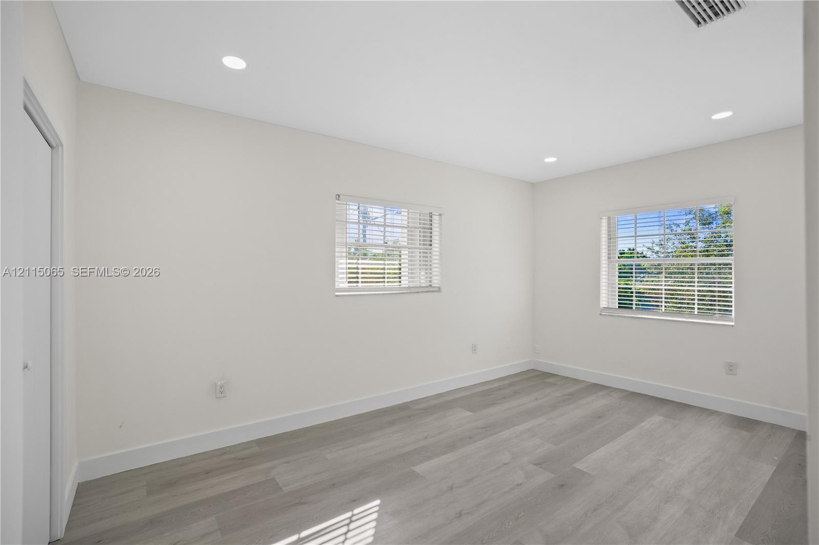 Neutral-toned interior featuring recessed lighting, wood-finish flooring, and multiple windows with horizontal blinds