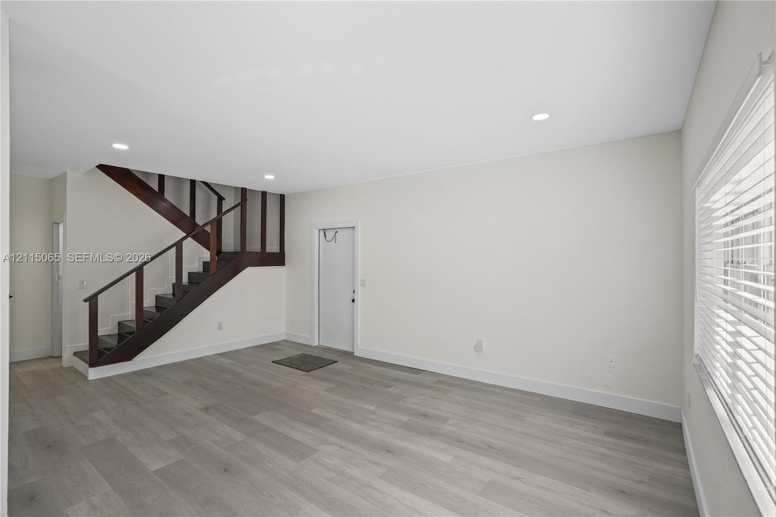 Open interior space featuring wood-finish flooring, recessed lighting, and a staircase with dark-toned railings and vertical slats