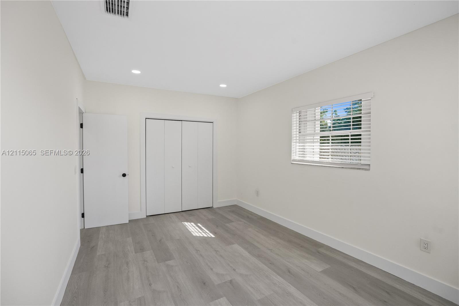 Neutral-toned interior featuring wood-finish flooring, recessed lighting, white walls, and a closet with bifold doors