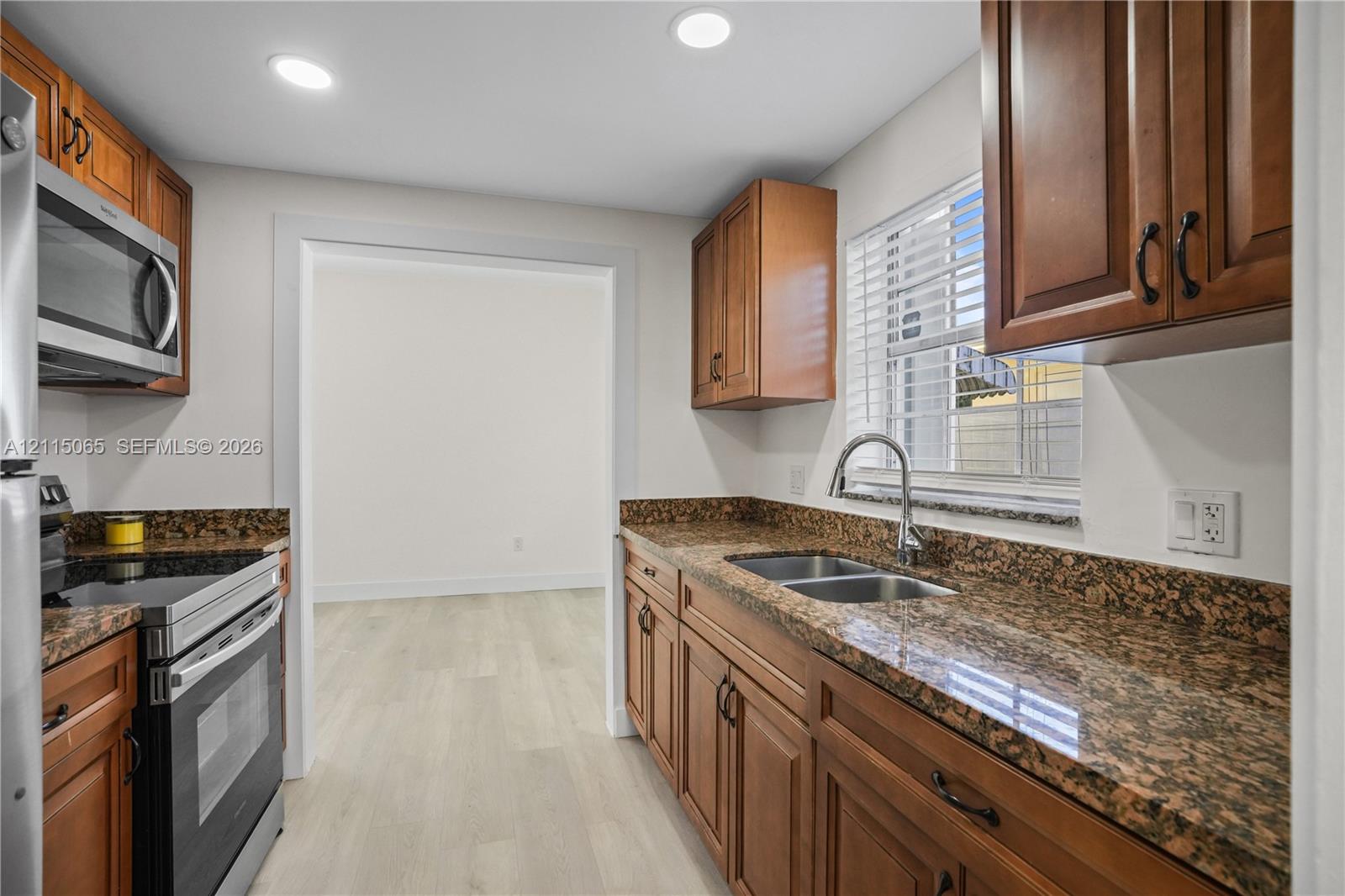 Kitchen featuring stained wood cabinetry, stone countertops, double-basin stainless steel sink, recessed lighting, and stainless steel appliances Kitchen featuring stained wood cabinetry, stone countertops, double-basin stainless steel sink, recessed lighting, and stainless steel appliances