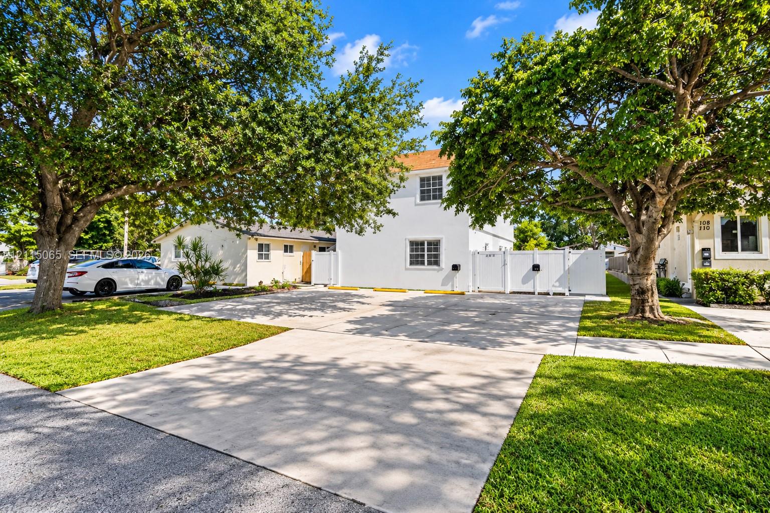 Exterior featuring a paved parking area, white privacy fencing, and mature canopy trees