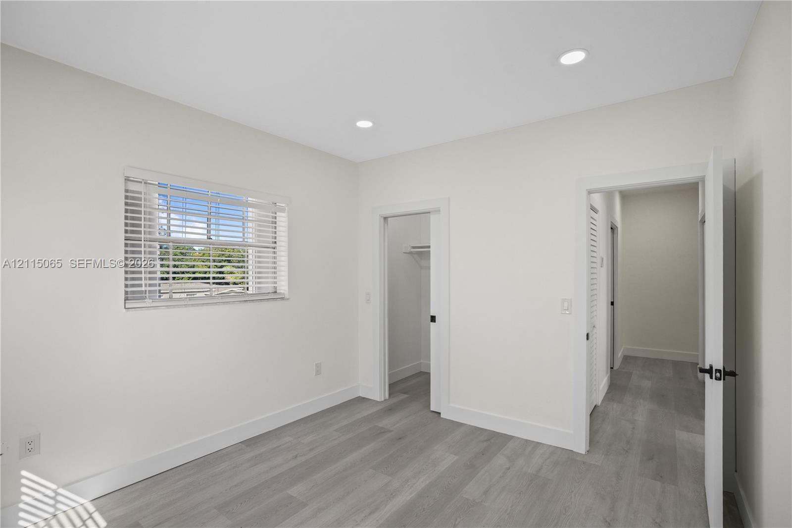Neutral-toned interior featuring wood-finish flooring, recessed lighting, a horizontal window with blinds, and built-in closet storage